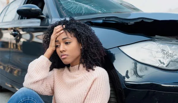 Mujer sentada junto a un coche tras un accidente