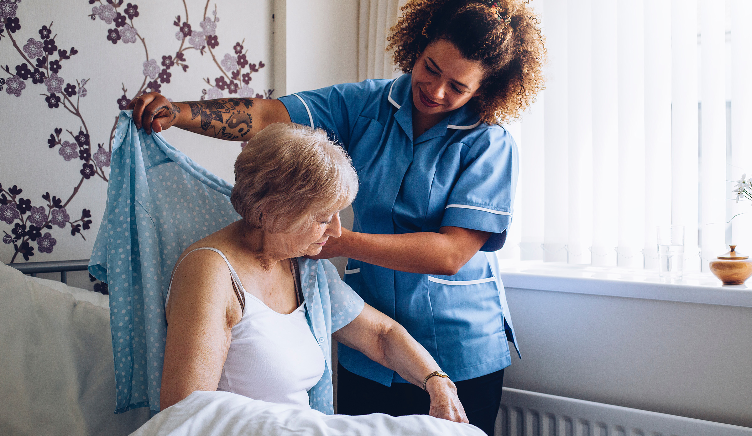 Asistente de una residencia de ancianos ayudando a vestirse a una residente