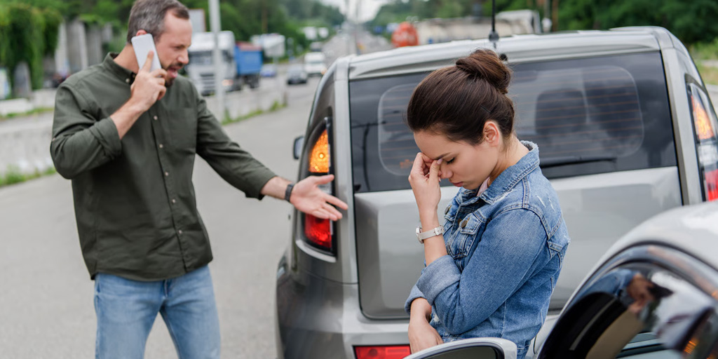 Man calling the police on the scene of a car accident, woman in the foreground